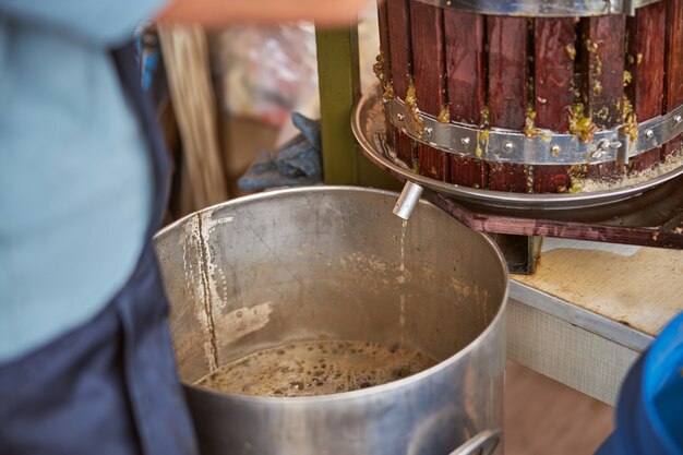 Foto recortada de jugo de uva que gotea de un tubo de prensa de vino en un recipiente de acero