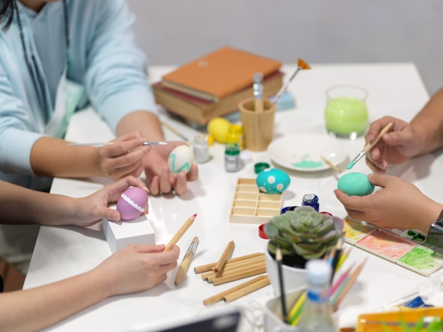 Foto recortada de manos de adolescentes pintando huevos de pascua, preparándose para el festival de pascua con herramientas de pintura