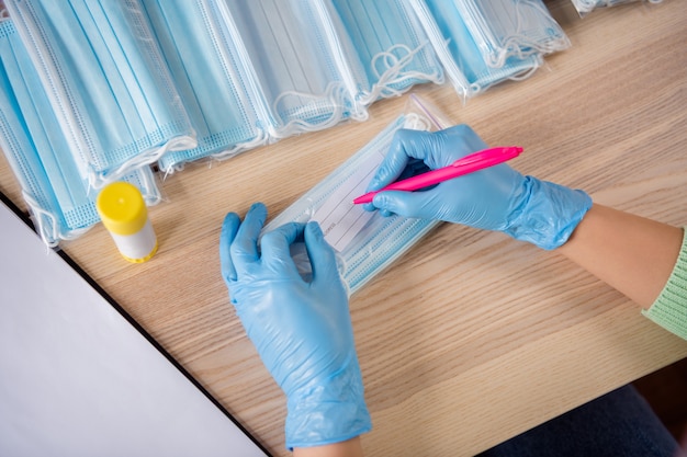 Foto recortada de manos guantes de látex tendencia negocio organizar orden cara máscaras médicas paquete de artesanía barra de pegamento poner escribir dirección del cliente tarjeta de papel preparar entrega oficina en casa en el interior