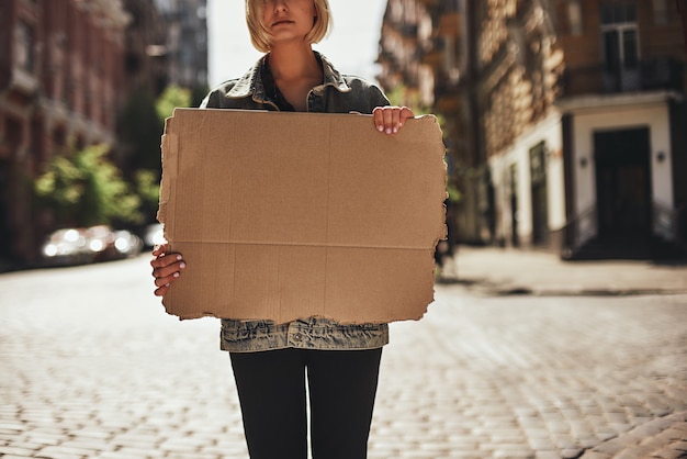 Foto recortada de mujer joven sosteniendo una pancarta en blanco mientras está de pie en la carretera vacía