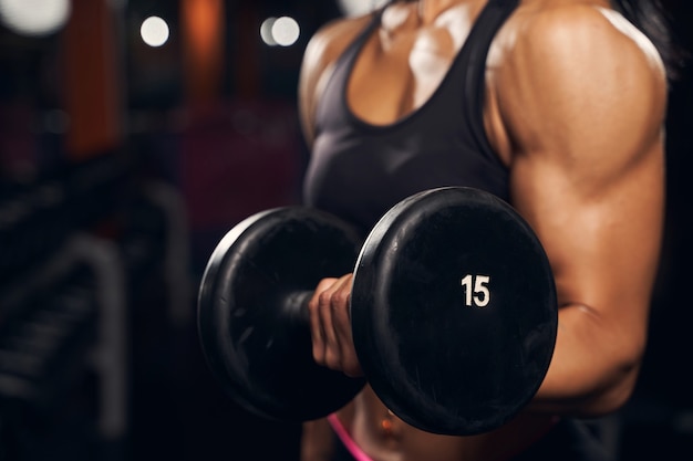 Foto recortada de mujer musculosa levantando pesas mientras hace ejercicio en el gimnasio