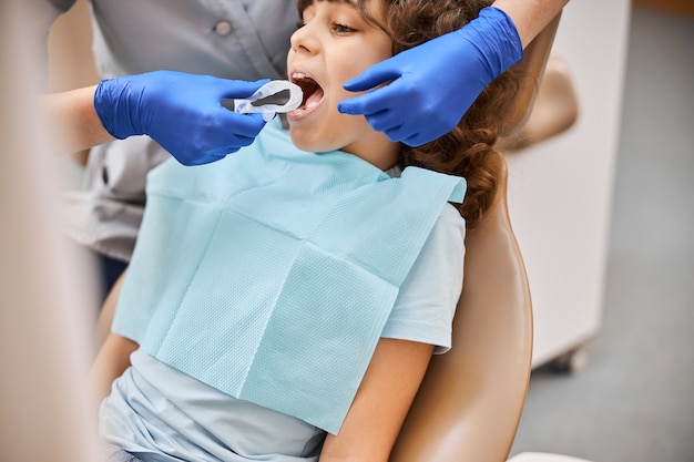 Foto recortada de un niño que abre la boca para que un dentista le inserte un dique de goma dental