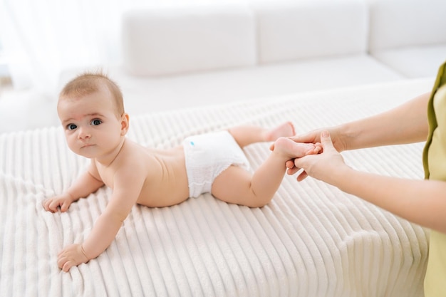 Foto recortada de una terapeuta femenina irreconocible haciendo gimnasia y masaje de pies a un adorable bebé en primer plano mano de enfermera haciendo ejercicios ortopédicos de piernas a un recién nacido