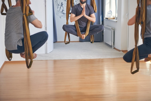 Foto recortada de tres personas caucásicas en forma descalza haciendo una pose de loto en la clase de yoga aérea