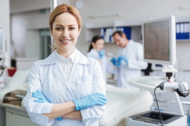 Foto de retrato. Asistente de laboratorio joven positivo cruzando los brazos sobre el pecho y manteniendo la sonrisa en la cara mientras se ve exitoso