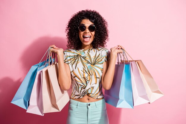 Foto de retrato de chica rizada de piel negra loca alegre manteniendo paquetes de compras aislados sobre fondo de color rosa pastel