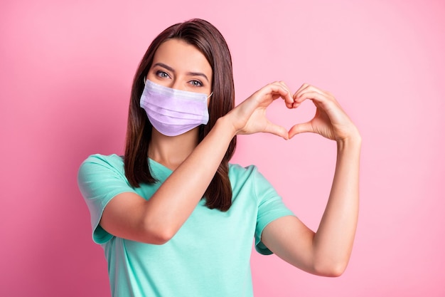 Foto retrato da namorada com as mãos em forma de coração no respirador de camiseta verde-azulado isolado em um fundo de cor rosa pastel