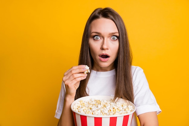 Foto retrato de menina chocada comendo pipoca assistindo filme de terror no cinema isolado fundo de cor amarela vívida