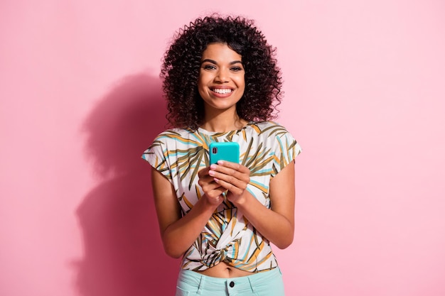 Foto retrato de mulher feliz segurando o telefone com as duas mãos, isolado em um fundo de cor rosa pastel