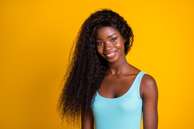 Foto retrato de uma garota afro-americana sorrindo usando uma regata azul isolada em um fundo amarelo vivo