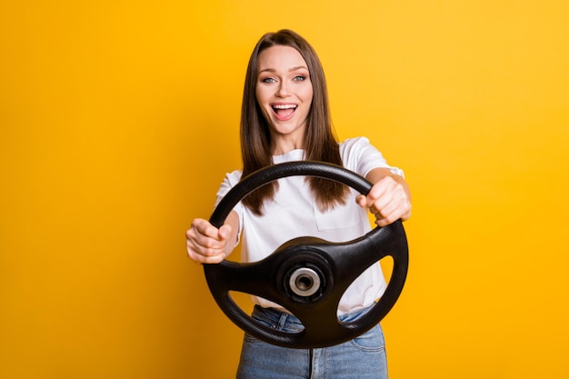 Foto foto retrato de uma menina linda morena mantendo o volante aprendendo a dirigir sorrindo isolado fundo de cor amarela vibrante