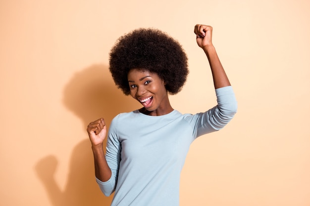 Foto retrato de uma mulher afro-americana dançando, sorrindo, rindo, isolada em um fundo de cor bege pastel
