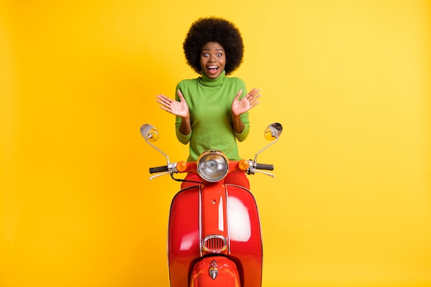 Foto retrato de mujer joven motociclista emocionado sorprendido mostrando dos manos aisladas sobre fondo de color amarillo vivo