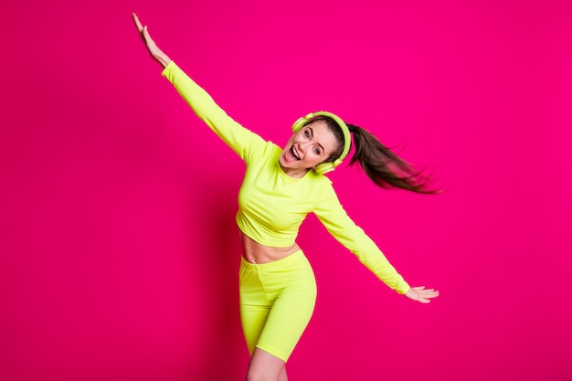 Foto de retrato de niña con auriculares sportwear fingiendo avión escuchando música aislado sobre fondo de color fucsia brillante