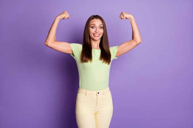 Foto retrato de niña fuerte mostrando bíceps aislado sobre fondo de color púrpura vivo