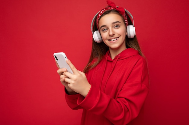 Foto de retrato en primer plano de la hermosa adolescente morena sonriente positiva vistiendo sudadera con capucha roja