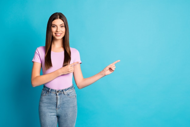 Foto retrato de radiante linda chica vistiendo camiseta púrpura casual apuntando con los dedos de dos brazos fondo de color azul aislado