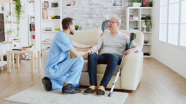 Foto reveladora de enfermero revisando a anciano jubilado con alzheimer sentado en un sofá en el hogar de ancianos