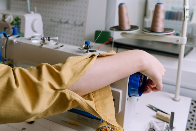 Foto sem rosto de mulher ajustando a máquina de costura antes de trabalhar na oficina de costura