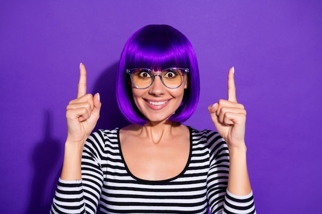 Foto de señora agradable indicando los dedos índices en el espacio vacío usar peluca pullover rayado fondo púrpura aislado