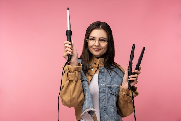 La foto de la señora atractiva sostiene la sonrisa feliz del pelo que se encrespa, viste el fondo de color rosado aislado de la camiseta blanca de la chaqueta de los pantalones vaqueros casuales.