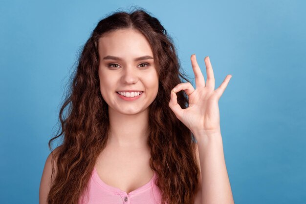 La foto de la señora bonita joven muestra los dedos okey símbolo gran perfecto decidir anuncio aislado sobre fondo de color azul.