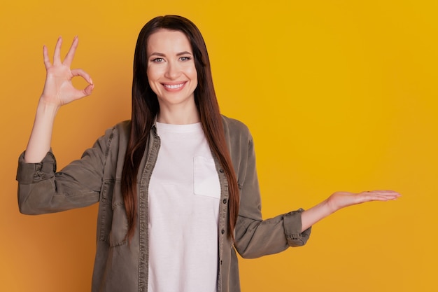 Foto de señora bonita mantenga abierta la palma de la mano mostrar ok ofrecer fondo amarillo aislado