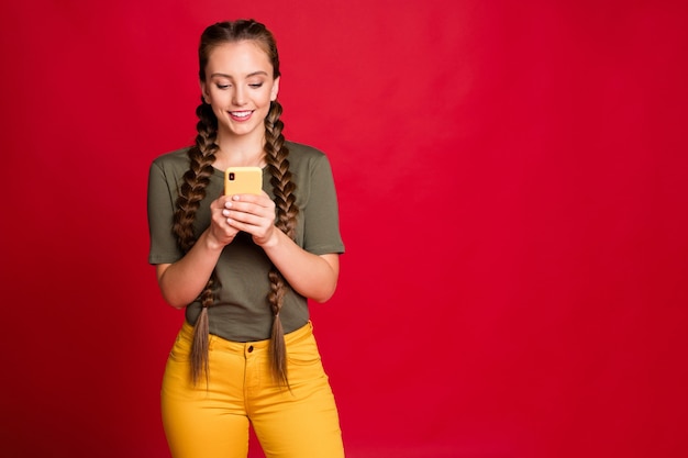 Foto de señora bonita trenzas largas sosteniendo las manos del teléfono leyendo nuevos comentarios positivos interesados usar pantalones amarillos casuales camiseta verde fondo de color rojo aislado