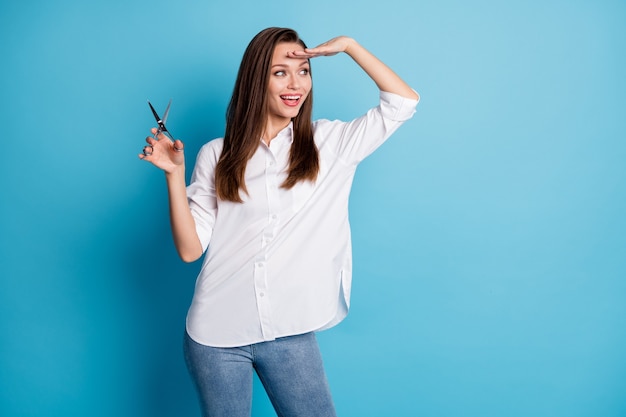 Foto de señora peluquería mantenga las tijeras mirar lejos esperando el salón del cliente desgaste camisa blanca jeans fondo de color azul aislado