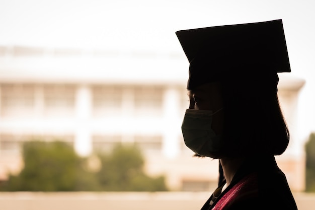 Foto de silueta de una joven mujer asiática feliz graduado universitario en toga de graduación