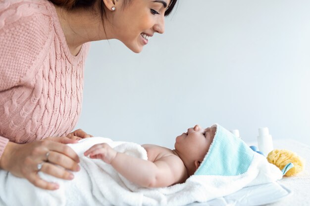 Foto de sonriente joven madre se divierte con el bebé después de bañarse en casa.