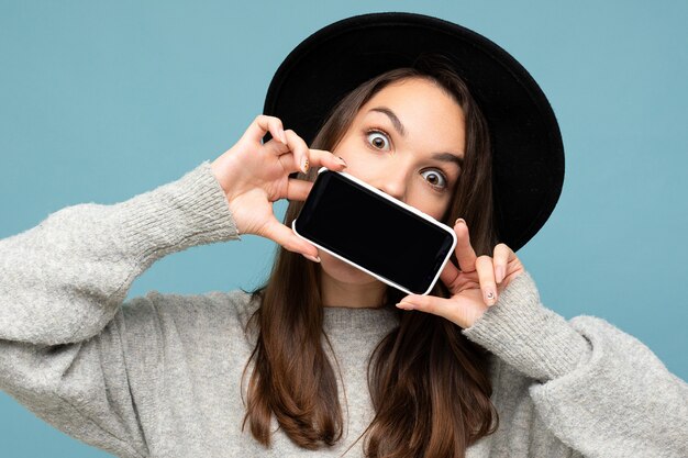 Foto de sorprendido conmocionado asombrado hermosa persona de sexo femenino joven positivo con sombrero negro y gris