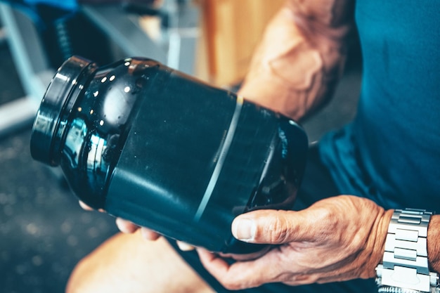 Foto de stock de un detalle de una botella de proteína en manos de un hombre musculoso en el gimnasio Fitness y deportes