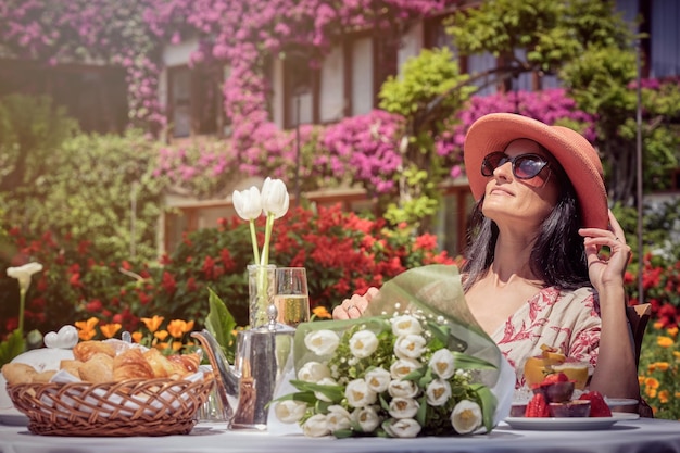 Foto de stock de una mujer feliz tomando el sol y disfrutando del desayuno en el jardín.