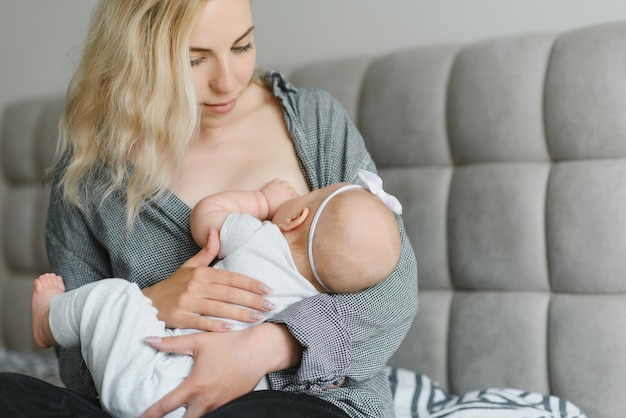 Foto suave joven madre amamantando a su bebé en casa en la habitación blanca