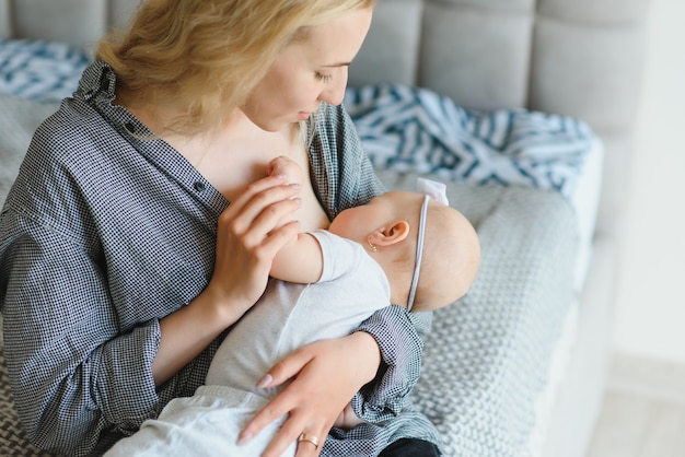 Foto suave joven madre amamantando a su bebé en casa en la habitación blanca