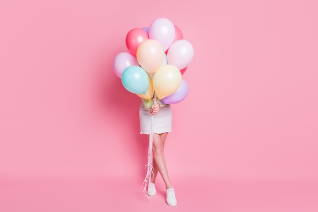 Foto de tamaño completo de una dama divertida, ven a la fiesta de cumpleaños, sostén muchos globos de aire, ocultando la cara, sorpresa, visita, usa, casual, verde, jersey, jeans, falda, zapatos, aislado, rosa, pastel, color, plano de fondo