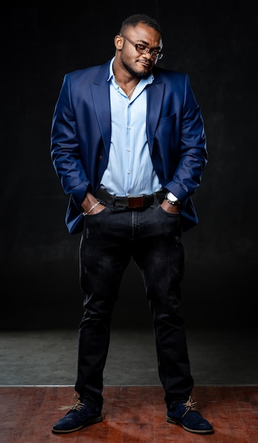 Foto de tamaño completo de un elegante joven apuesto hombre de negocios afroamericano, director ejecutivo, gerente con gafas y traje mirando directamente con las manos en los bolsillos. Retrato de moda de estudio. De cerca.