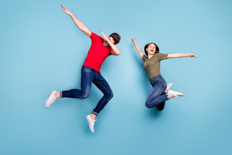 Foto de tamaño completo de funky locos dos personas casadas estudiantes diversión salto hombre realizar dab bailarines mujer levantar manos usar camiseta verde rojo jeans zapatillas de deporte aislado fondo de color azul