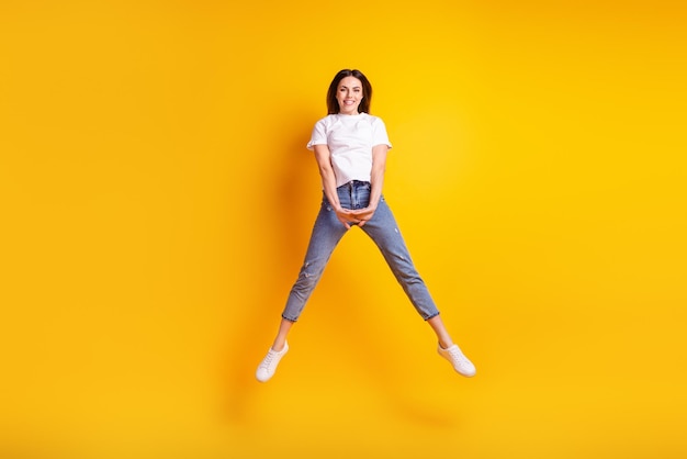 Foto a tamaño completo de una joven guapa de buen humor salta enérgica aislada sobre un fondo de color amarillo