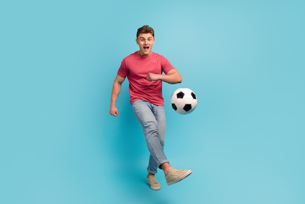Foto a tamaño completo de un joven que juega al fútbol patada en el campeonato de juegos de equipo aislado sobre un fondo de color azul