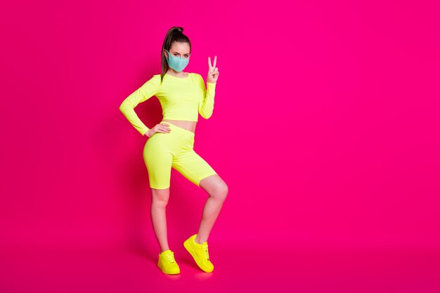 Foto del tamaño del cuerpo de longitud completa de una niña con zapatillas deportivas que muestran un gesto de signo v aislado sobre fondo de color fucsia brillante