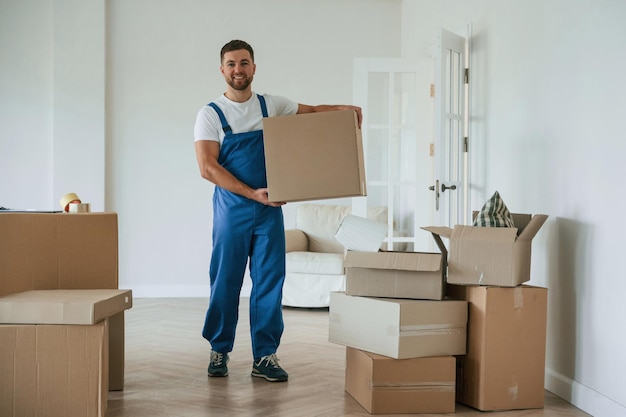 Foto foto a toda altura de pie y sosteniendo una caja grande empleado de servicio en movimiento en una habitación