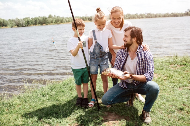 Una foto de toda la familia parada en la hierba y mirando los peces que papá atrapó. Los niños y la mujer parecen asombrados. Son felices. El hombre los mira y sonríe.