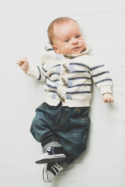 Foto de tonos de lindo bebé en jeans y suéter acostado en la cama