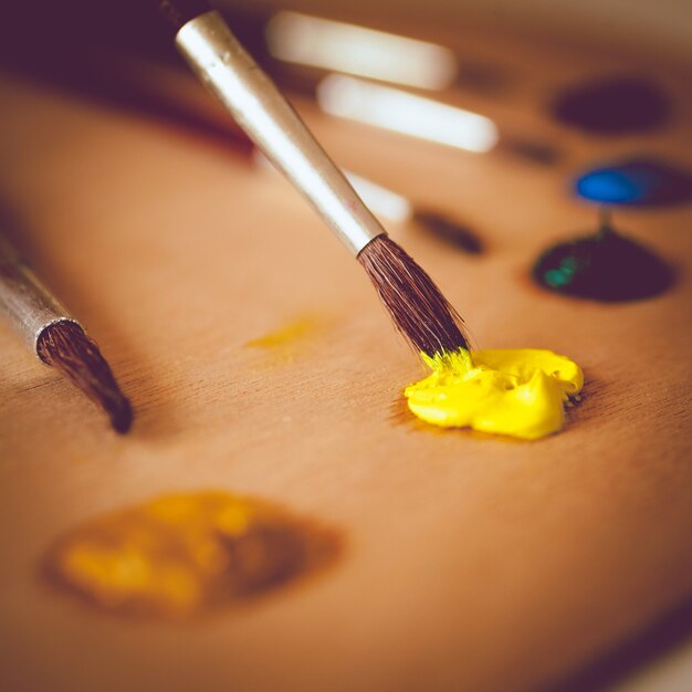 Foto en tonos de primer plano de pincel sumergido en pintura de aceite de color amarillo vivo