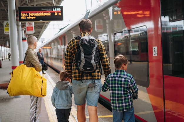 Foto traseira do homem caucasiano segurando as mãos das crianças andando pela plataforma indo pegar o trem