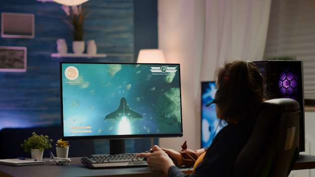 Foto traseira do jogador profissional jogando jogo de tiro espacial on-line em um computador poderoso usando o controle sem fio. mulher cibernética competitiva realizando torneio de videogame usando joystick profissional