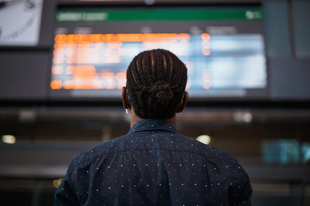 Foto trasera del hombre africano mirando el horario de llegadas y salidas en la estación de tren
