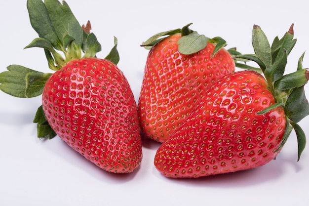 Foto de tres fresas rojas frescas con hojas de fresa aisladas sobre superficie blanca